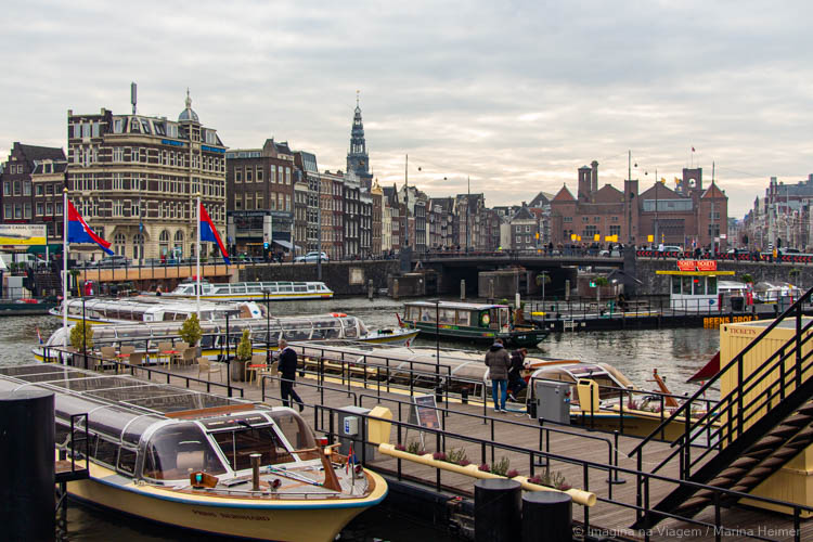 Barcos de passeio atracados perto da Amsterdam Centraal, com prédios históricos do centro ao fundo