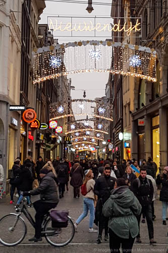 Nieuwendijk movimentada e decorada, com pedestres, bicicletas e lojas no centro de Amsterdam